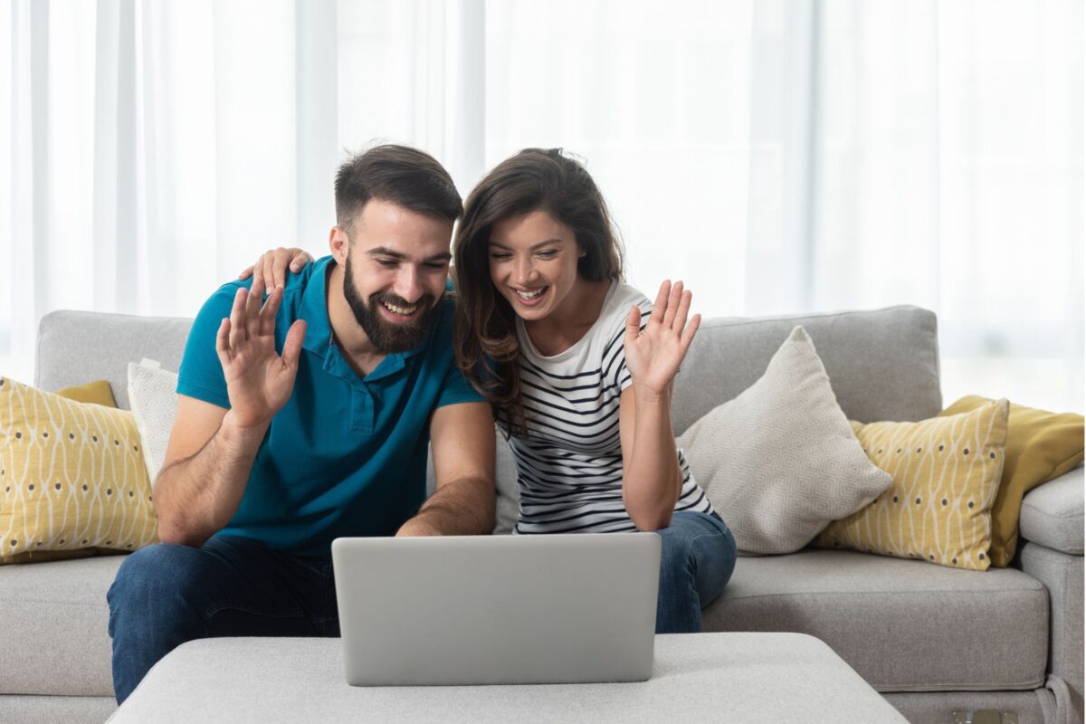 Couple looking at a laptop smiling and waving.